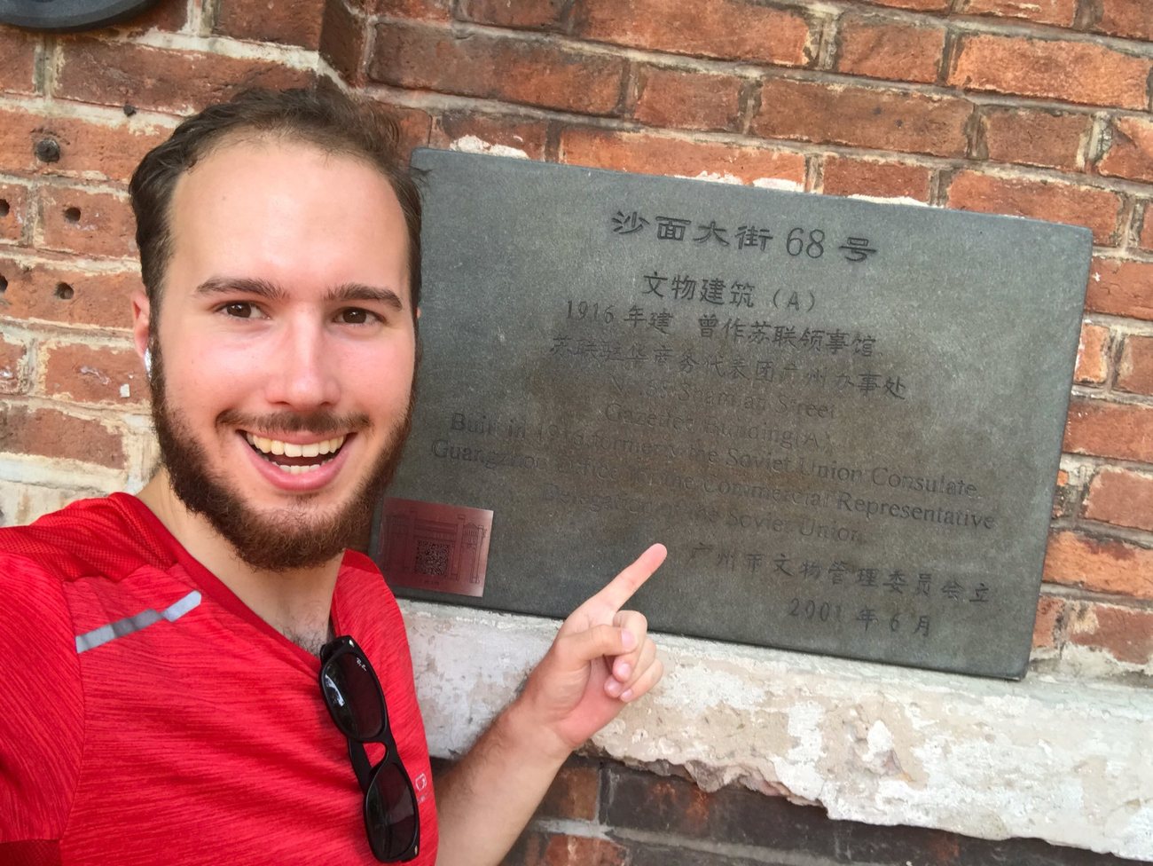 2019年，一位穿红衣的年轻男子在铭牌前自拍，手指着铭牌
